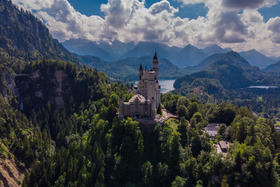 Aerial view of Neuschwanstein Castle, nestled in the lush Bavarian forest with mountain backdrop.